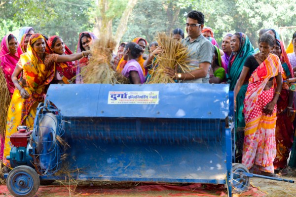Women villagers participate in a demonstration of an open-drum thresher.